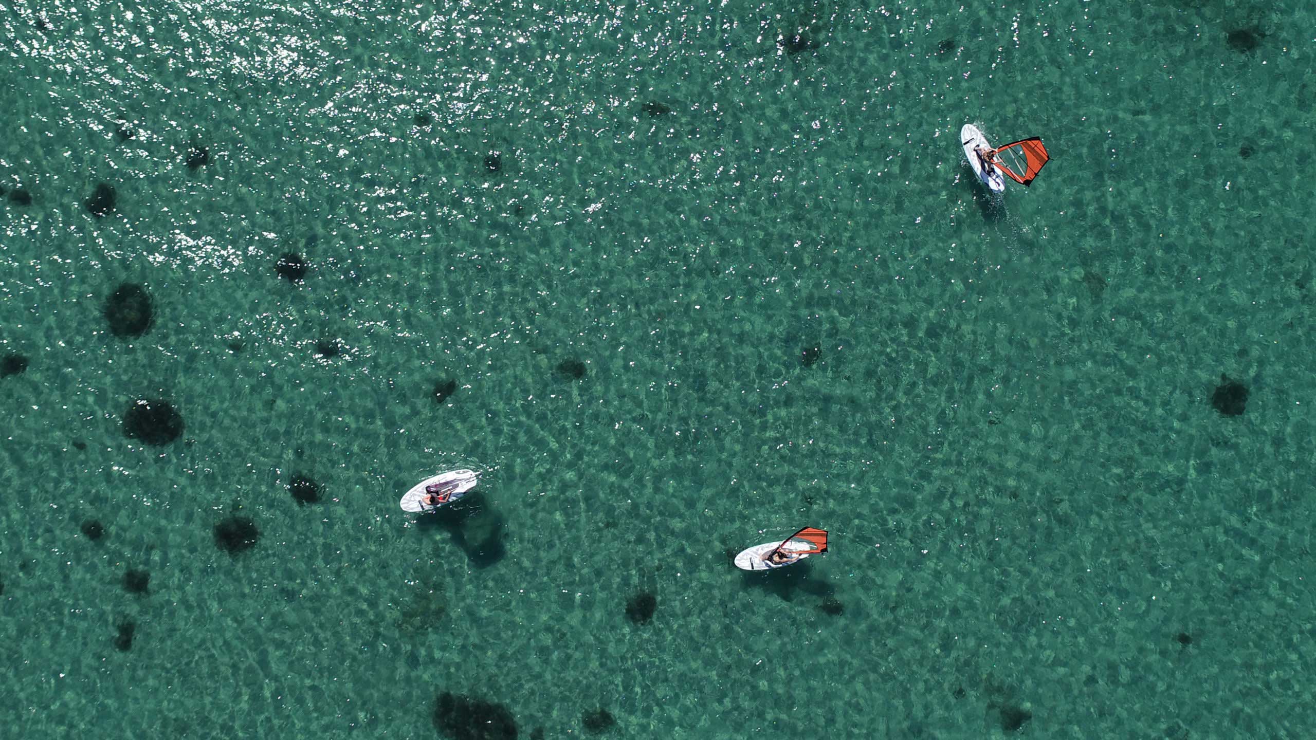 Three people windsurfing on blue waters